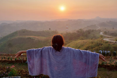 Rear view of carefree woman with arms outstretched looking at sunset