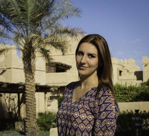 Portrait of young woman standing against tree