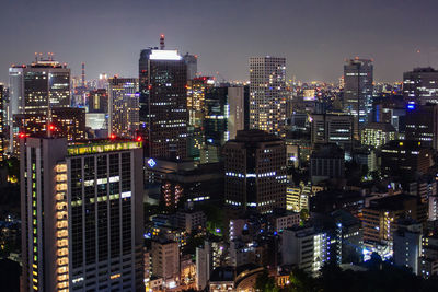 Illuminated modern buildings in city against sky at night