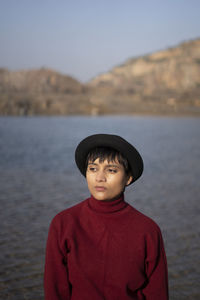 Young woman looking away while standing by lake