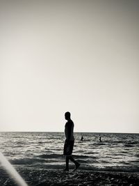 Rear view of man standing at beach against clear sky