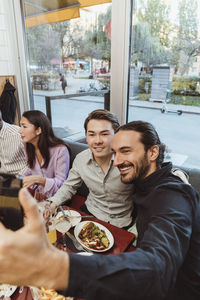 Smiling man taking selfie with male friend in bar