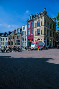 Buildings by street in city against blue sky