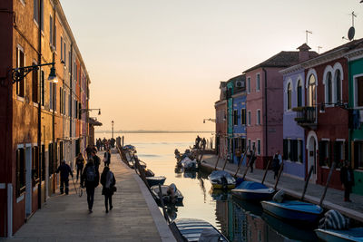 People walking on street by canal against sea