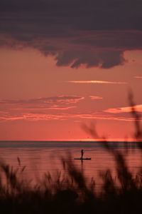 Scenic view of sea against purple and rosy sky at sunset with a woman on a sup board in the distance