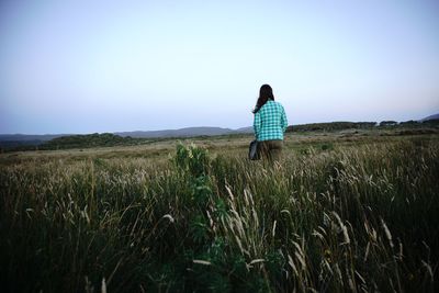 Rear view of woman walking on field against clear sky