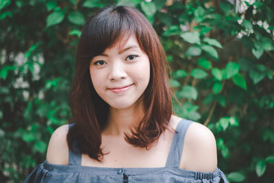 Portrait of smiling young woman standing against tree