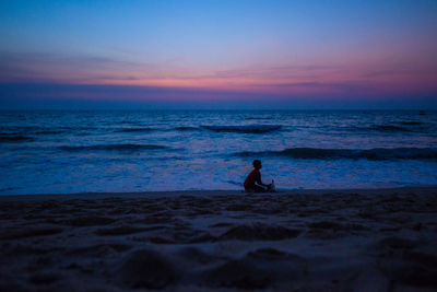 Silhouette boy playing at beach against sky during sunset