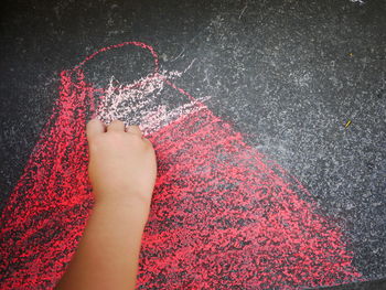 Cropped hand of child drawing with chalk on asphalt