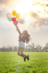 Full length of man holding balloons on field against sky