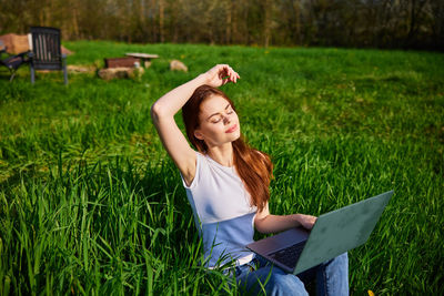 Young woman using laptop while sitting on field