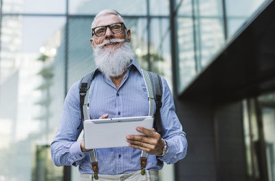 Senior hipster holding digital tablet against building