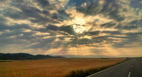 Road passing through field against cloudy sky