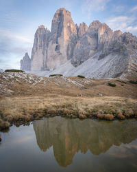 Sun setting over massive rock formation of tre cime reflecting in small pond,dolomites,vertical shot