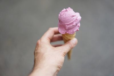 Male hand holding ice cream cone against gray background