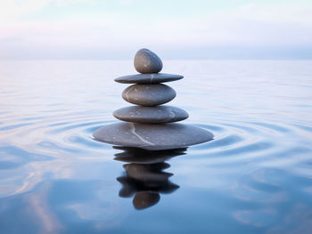 Stack of stones in sea against sky