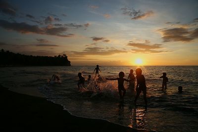 Silhouette people standing on beach against sky during sunset