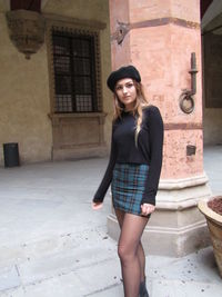 Portrait of young woman standing against building