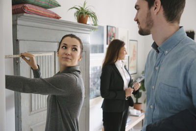 Man looking at woman holding tape measure with female realtor in background