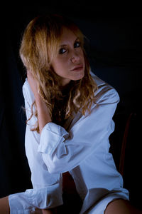 Portrait of mid adult woman sitting on chair against black background