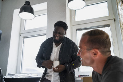 Cheerful multiracial carpenters having fun during coffee break in apartment