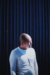 Young man looking away while standing against blue background