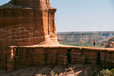 View of rock formation against sky with one single figure of a person walking towards the formation