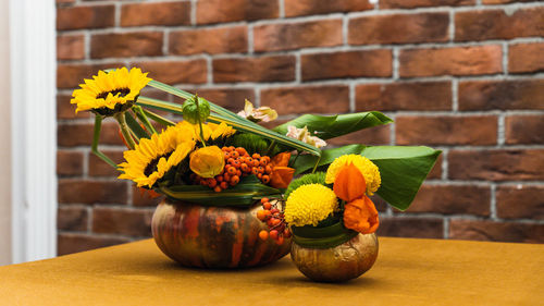 Close-up of yellow flower pot on table against brick wall