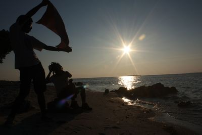 Silhouette people on beach against sky during sunset