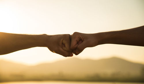 Midsection of couple hands against sky during sunset