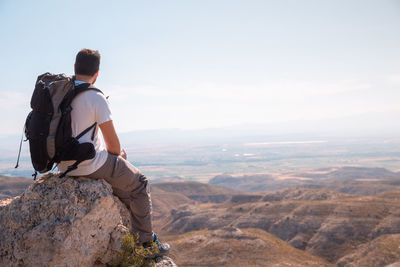 Man sitting on rock against mountains and sky