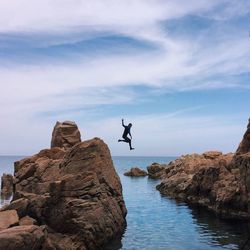 Man jumping in sea against cloudy sky