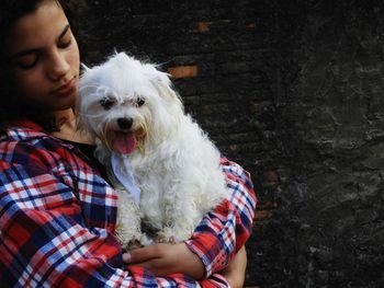 Young woman carrying dog while standing against wall