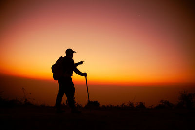 Hiker with backpack relaxing on top of a mountain and enjoying valley view during sunrise