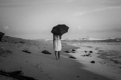 Rear view of woman walking at beach against sky