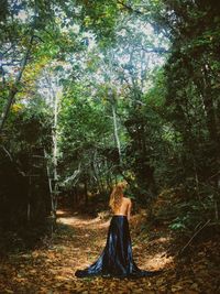 Rear view of shirtless woman wearing skirt while standing amidst forest