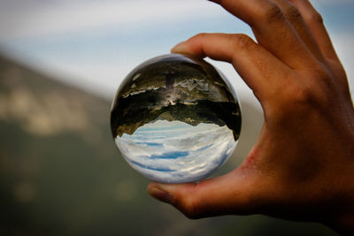 Close-up of human hand holding crystal ball against sky
