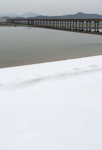 Bridge over snow covered land against sky