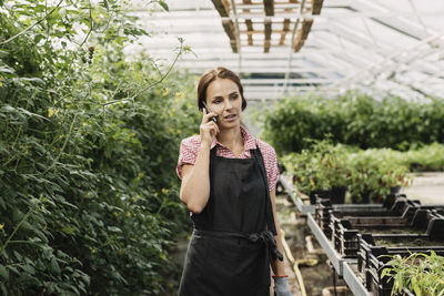 Female gardener talking on mobile phone in greenhouse