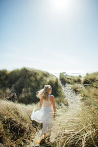 Rear view of young woman walking on trail leading towards beach