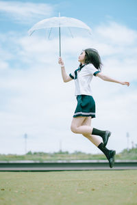 Side view of young woman with umbrella jumping in park