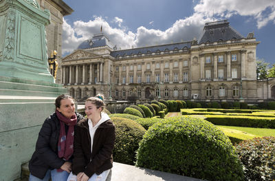 Mother and daughter sitting on railing against historic building in city