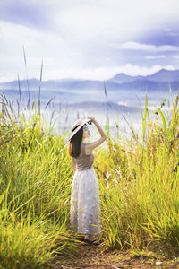 Rear view of woman standing on field against sky