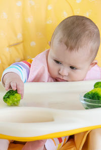 Cute baby girl playing with broccoli at home