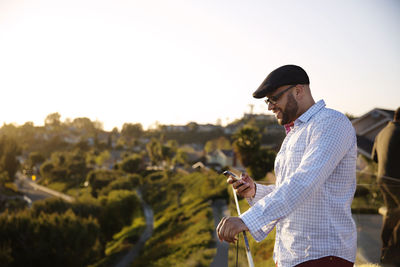 Side view of man using smart phone while standing by railing of balcony