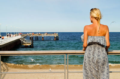 Rear view of woman standing on bridge by railing against sea