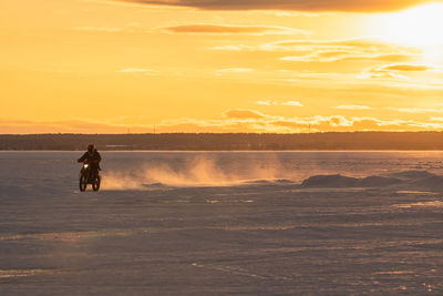 Motocrosso on frozen lake against sky during sunset
