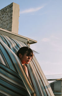 Low angle view of young woman looking away against sky