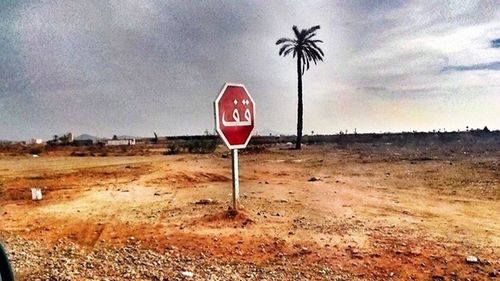 Road sign on field against sky