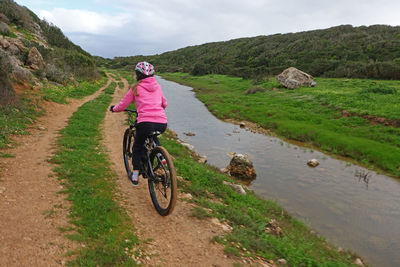 Girl on mountain bike cycling along a dirt track next to a river